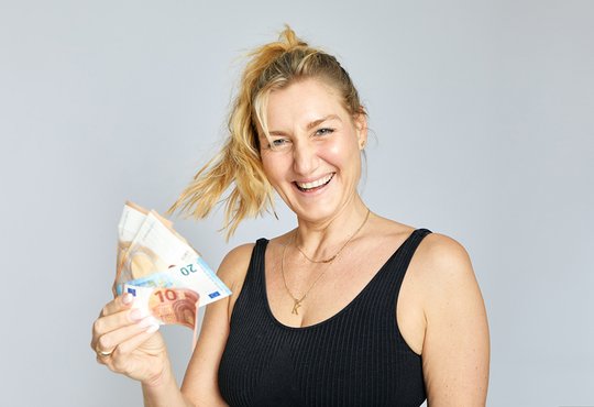 sportliche glueckliche blonde frau haelt geld in der hand kostenloser online praeventionskurs krankenkasse zahlt